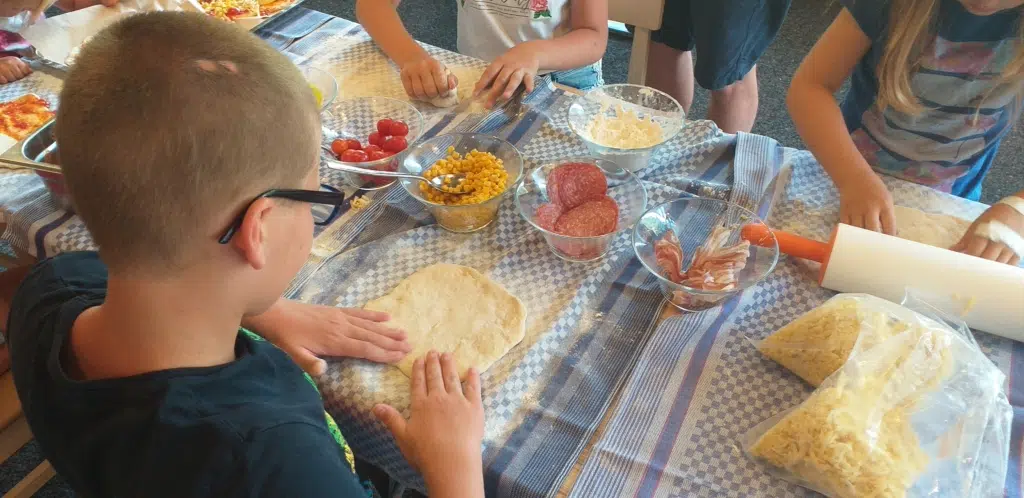 Ihr seht Kinder beim Backen einer Pizza. JUFA Kids-Club bietet Spaß und Aktion und ist im Urlaub inklusive.