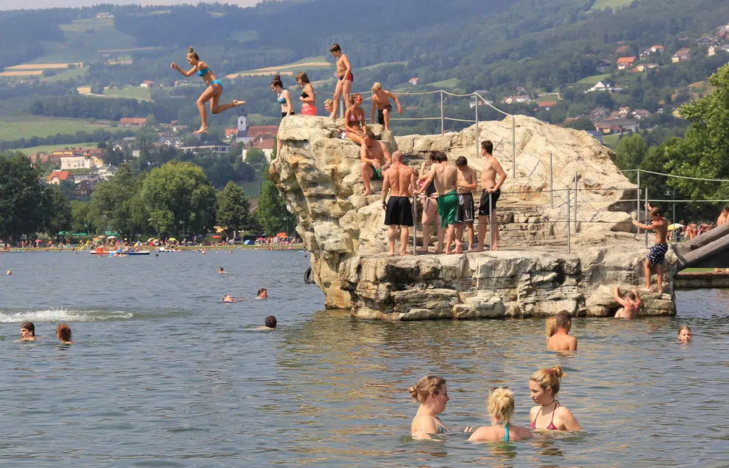 Jugendliche springen vom Sprungfelsen in das kühle Nass vom Stubenbergsee in der Steiermark. JUFA Hotels bietet tollen Sommerurlaub an schönen Seen für die ganze Familie.