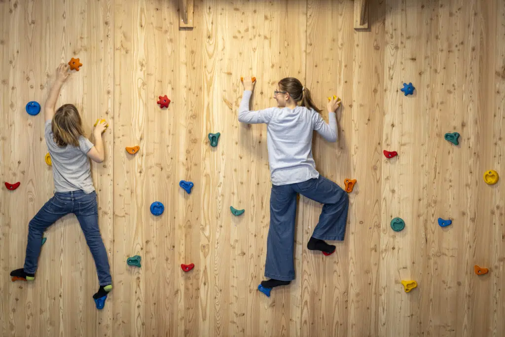 Ihr seht zwei Kinder, die gerade die hölzerne Boulderwand im Indoor-KInderspielbereich im JUFA Hotel Bad Radkersburg erklimmen.