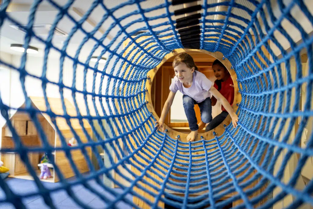 Ihr seht zwei junge Mädchen beim Krabbeln in einer Seilbrücke im Indoor-Kinderspielbereich des JUFA Hotel Bad Radkersburg.