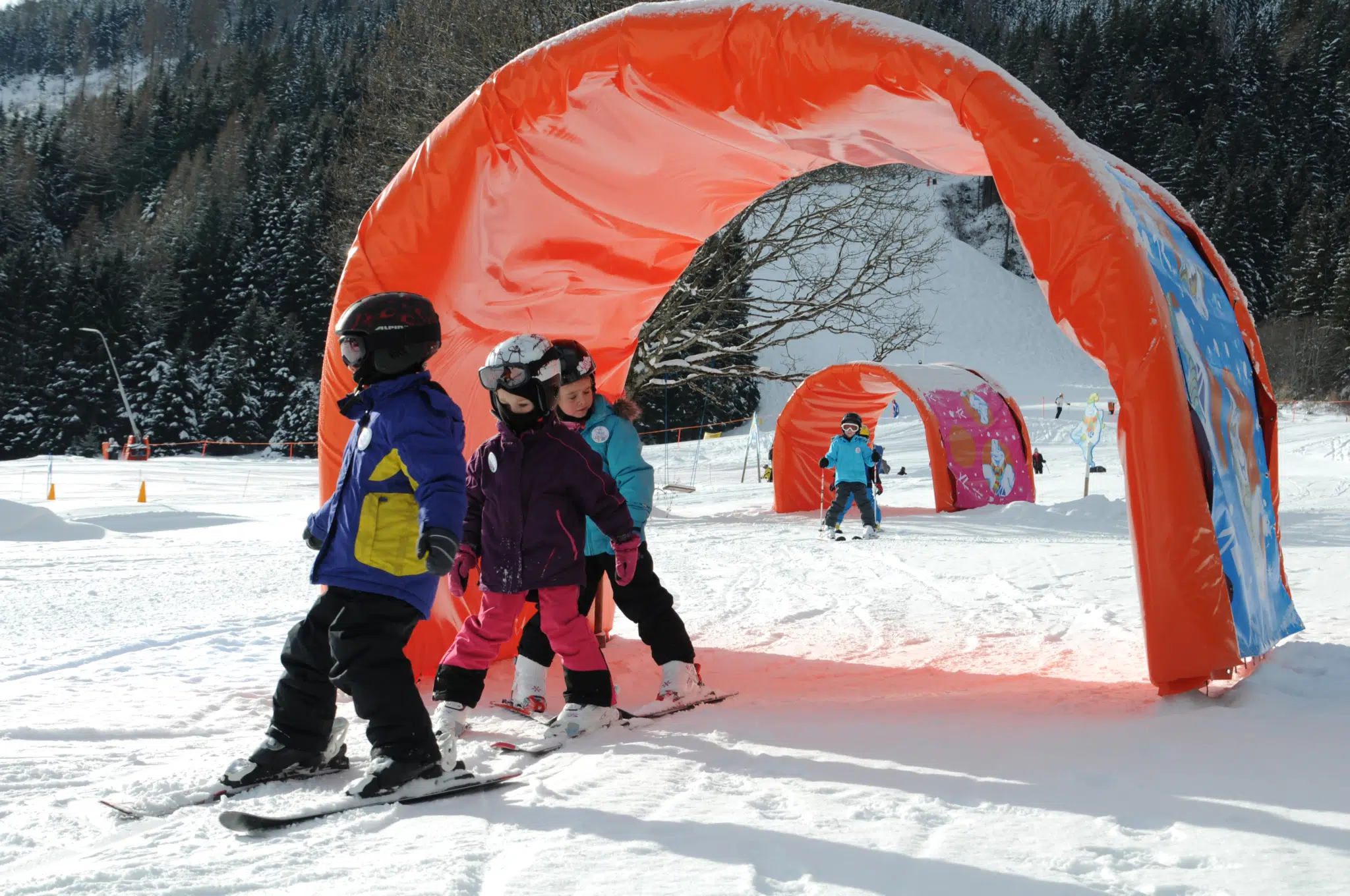 Kinder beim Skifahren auf der Krispini Tunnel-Piste in der Kinderskischaukel im Skigebiet Riesneralm. JUFA Hotels bietet erholsamen Familienurlaub und einen unvergesslichen Winterurlaub.