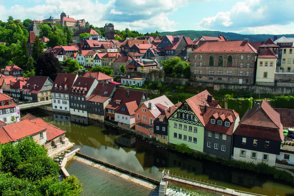 Ihr seht Kronach mit einem Fluss und der Festung Rosenberg im Sommer. JUFA Hotels bietet kinderfreundlichen und erlebnisreichen Urlaub für die ganze Familie.