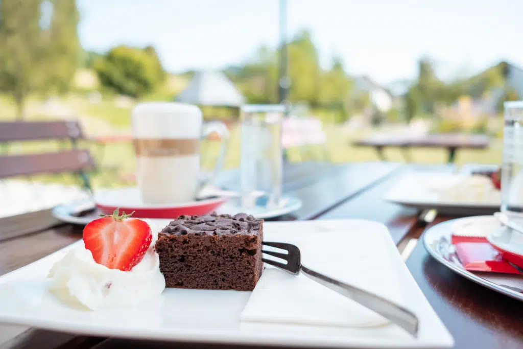 Ihr seht ein Stück Schokokuchen mit Erdbeere auf Sahne im Cafe im Garten. JUFA Hotels bietet erholsamen Familienurlaub und einen unvergesslichen Winter- und Wanderurlaub.