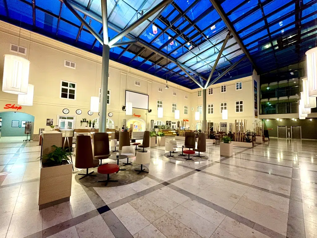 Ihr seht die Innenhof-Lobby mit Bar- und Rezeptionsbereich im JUFA Hotel Wien-City. Der Ort für erholsamen Städteurlaub in Österreich.