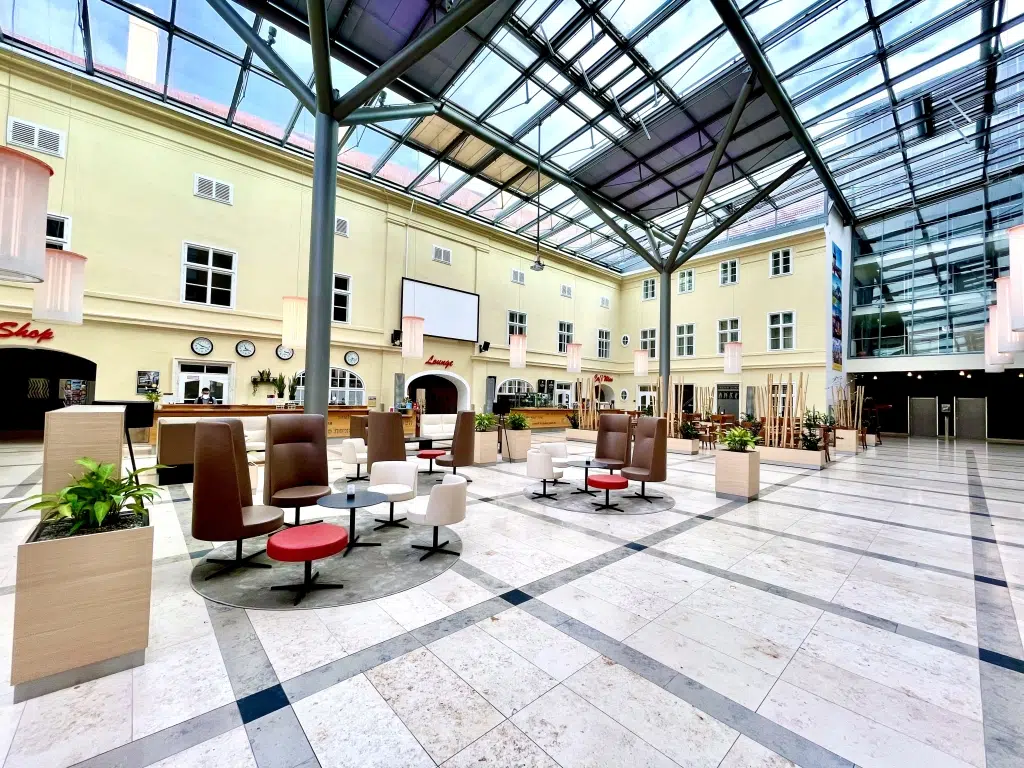 Ihr seht die Innenhof-Lobby mit Bar- und Rezeptionsbereich im JUFA Hotel Wien-City. Der Ort für erholsamen Städteurlaub in Österreich.