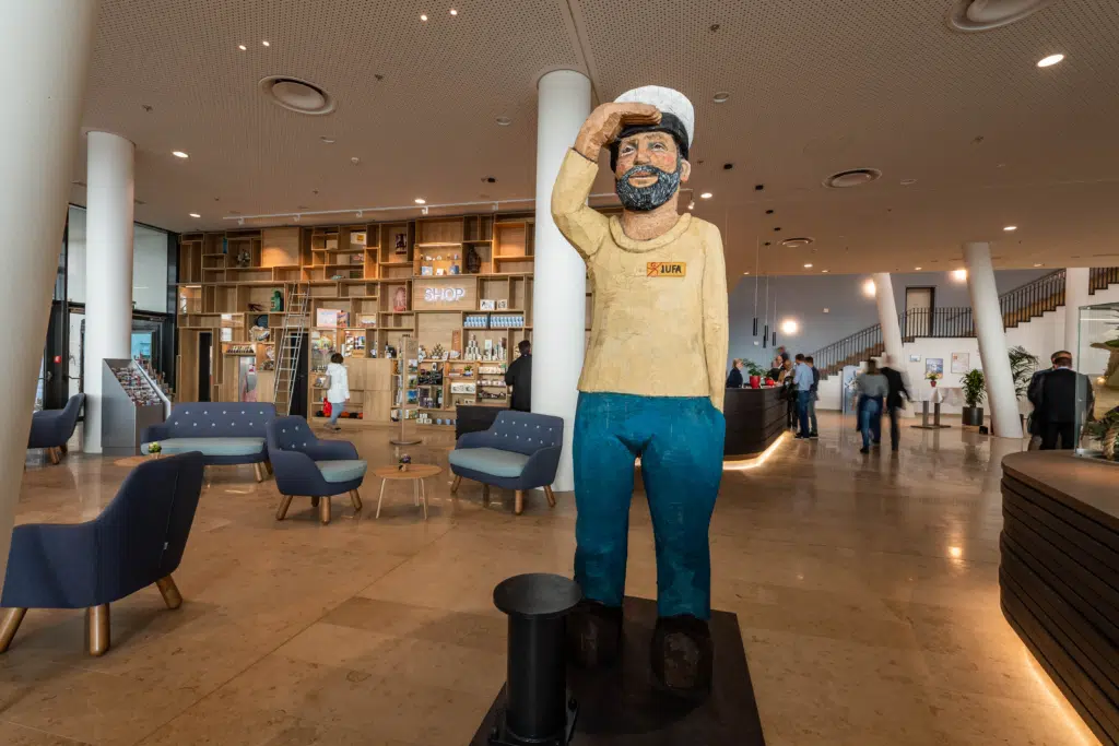 Ihr seht die Lobby mit einer Seemannsstatue im JUFA Hotel Hamburg HafenCity****. Der Ort für erlebnisreichen Städtetrip für die ganze Familie und der ideale Platz für Ihr Seminar.