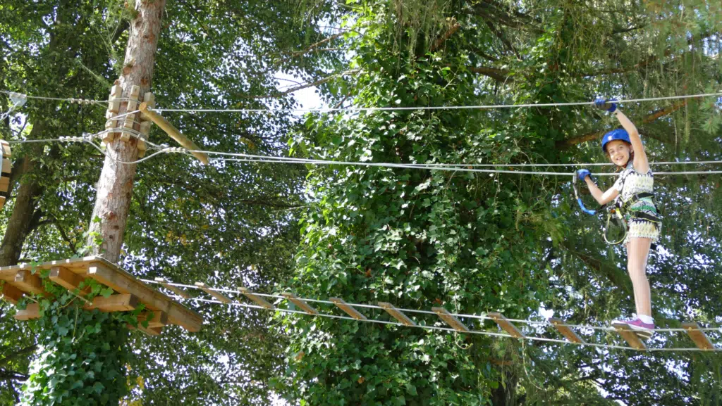 Ein Mädchen geht im Hochseilgarten im Freizeitpark Stubenbergsee über eine Seilbrücke. JUFA Hotels bieten erholsamen Familienurlaub und einen unvergesslichen Winter- und Wanderurlaub.