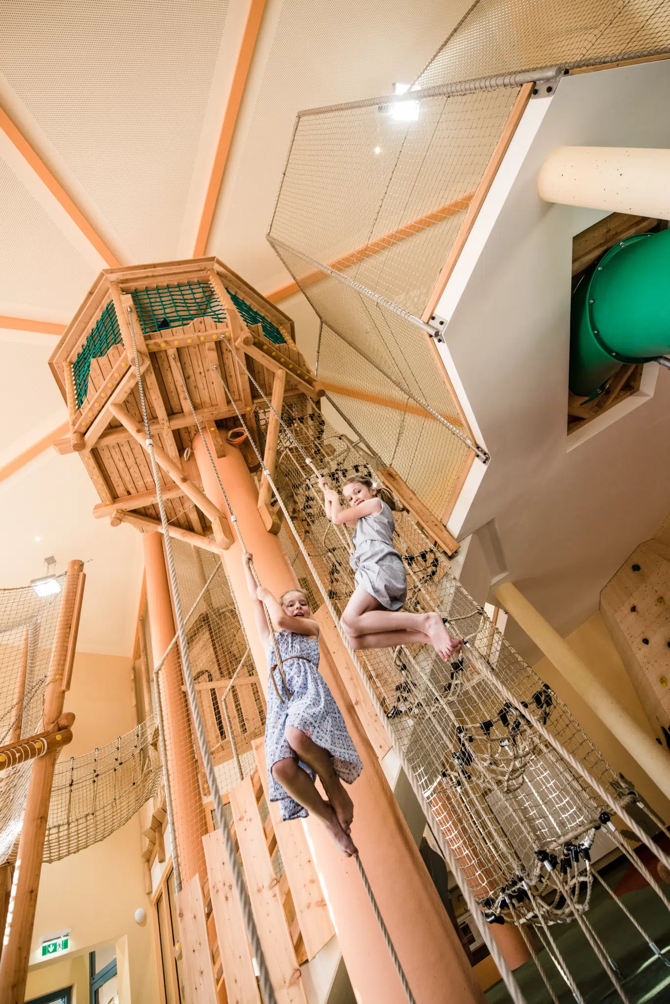 Ihr seht zwei Mädchen auf den Kletterturm im JUFA Hotel Stubenbergsee klettern. JUFA Hotels bietet kinderfreundlichen und erlebnisreichen Urlaub für die ganze Familie.