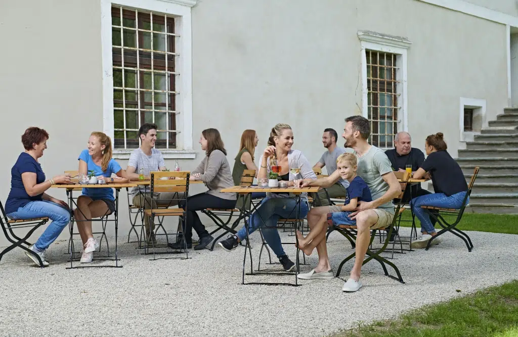 Ihr seht Menschen auf der gemütlichen Sonnenterrasse im JUFA Hotel Stift Gurk im Sommer. JUFA Hotels bietet den Ort für erlebnisreichen Natururlaub für die ganze Familie.