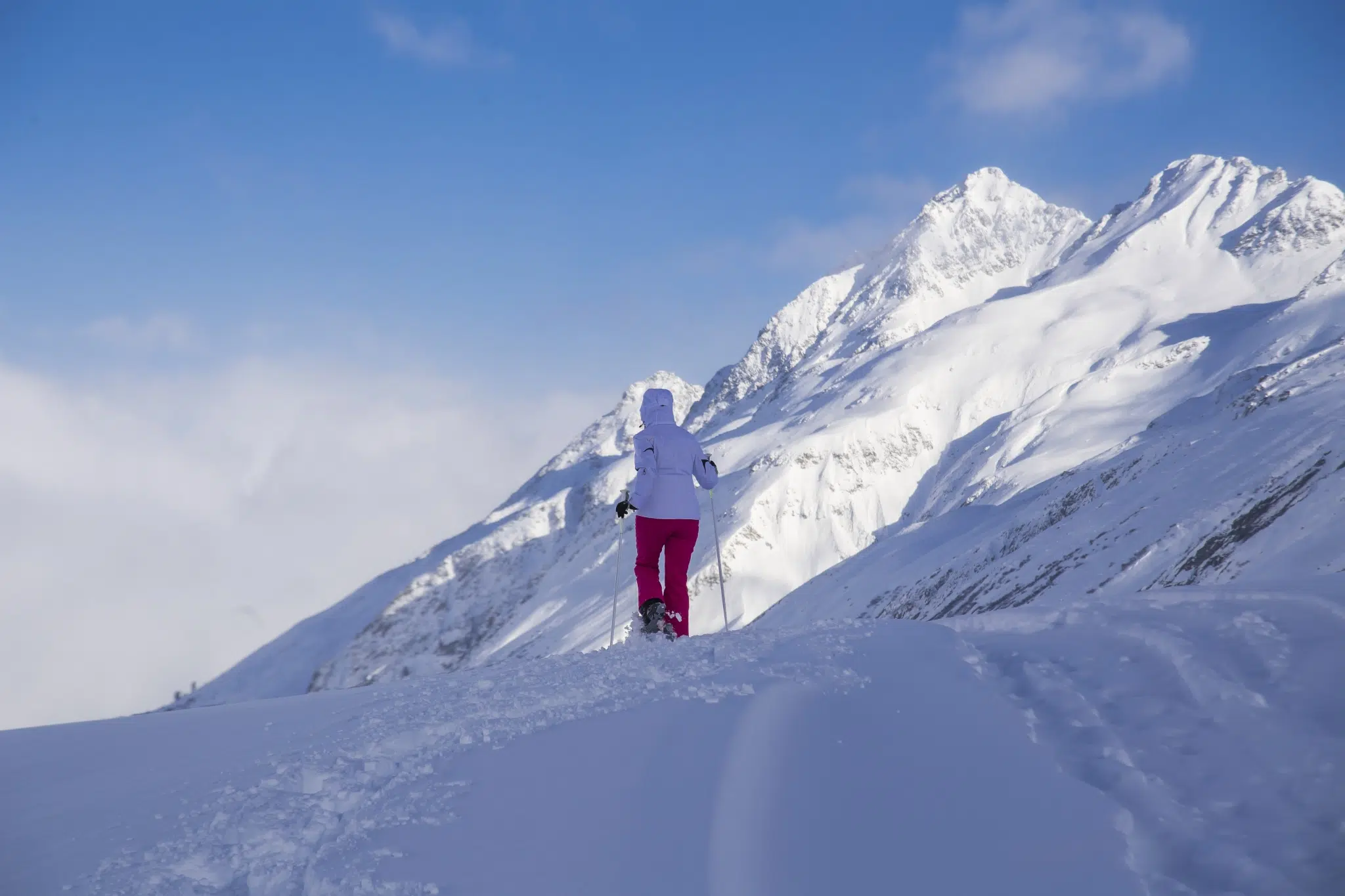 Frau beim Schneeschuhwandern im Montafon vor verschneiten Berggipfeln. In der Nähe des JUFA Hotel Montafon. Der Ort für erholsamen Familienurlaub und einen unvergesslichen Winterurlaub.