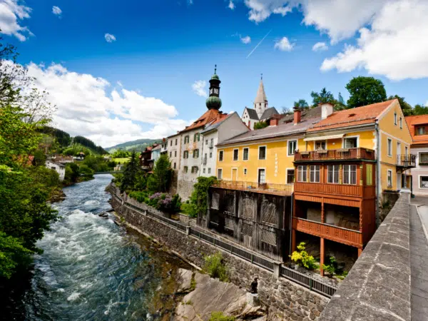 Ihr seht die Mur in Murau mit dem Rathaus und der Stadtpfarrkirche im Sommer. JUFA Hotels bietet erholsamen Familienurlaub und einen unvergesslichen Winter- und Wanderurlaub.