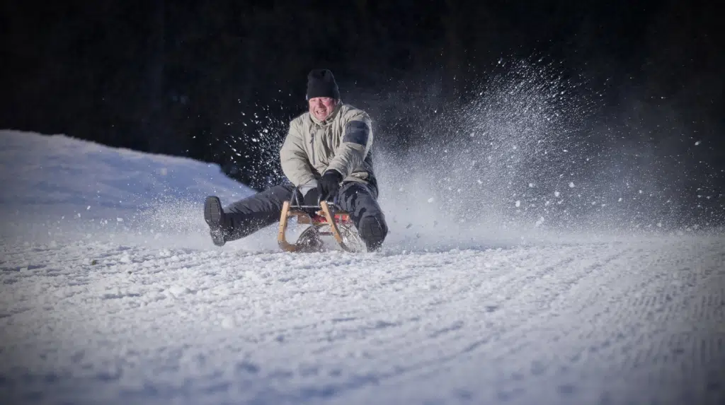 Ihr seht einen Mann mit Schlitten auf der Nachtrodelbahn Grafenwiese Tauplitz rodeln. JUFA Hotels bietet erholsamen Familienurlaub und einen unvergesslichen Winter- und Wanderurlaub.