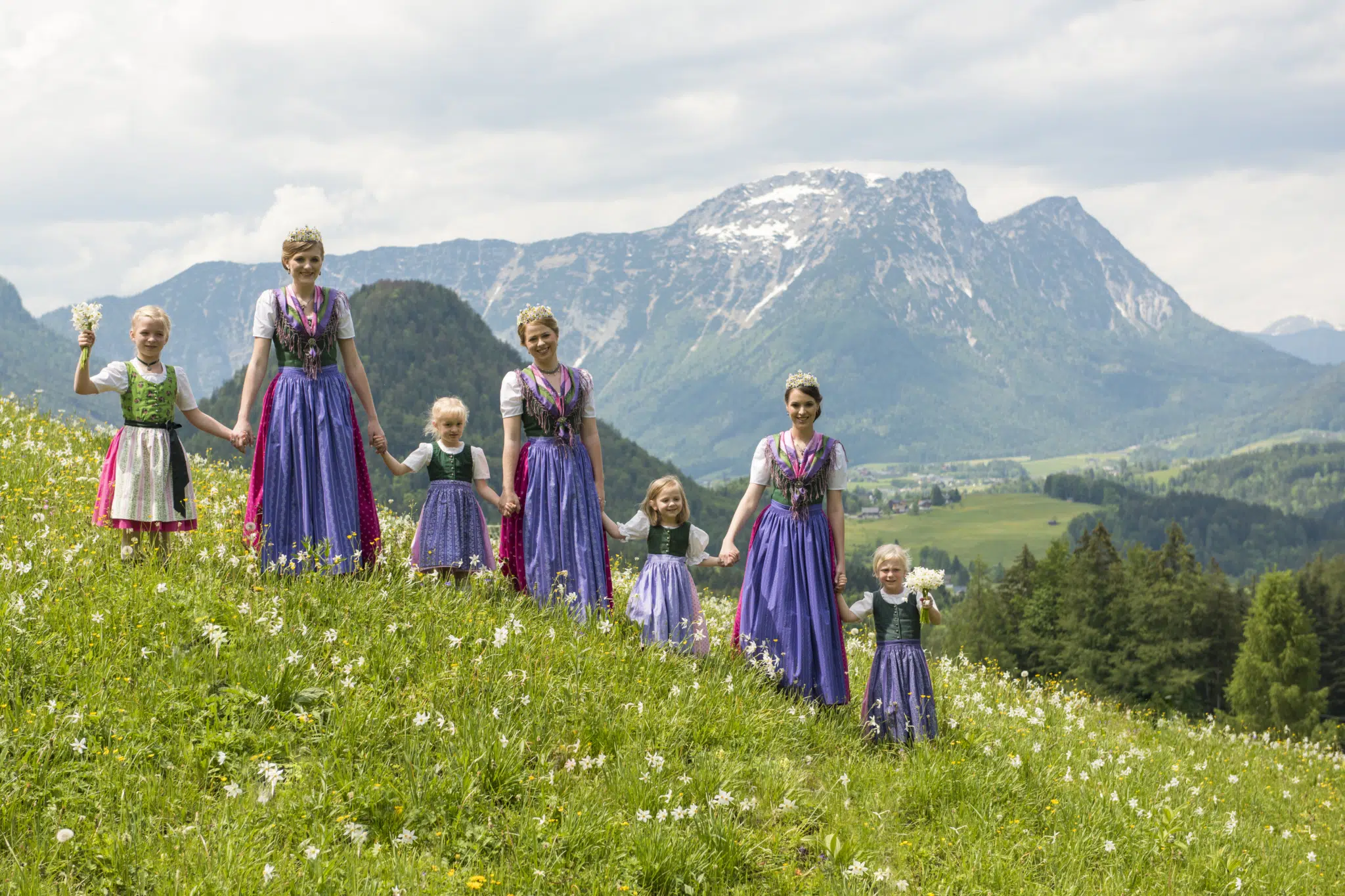 Ihr seht die Narzissenkönigin mit den Prinzessinnen und Kindern in einer Blumenwiese. JUFA Hotels bietet kinderfreundlichen und erlebnisreichen Urlaub für die ganze Familie.