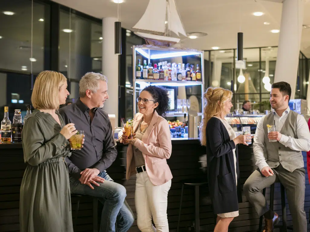 Ihr seht Frauen und Männer beim Networken an der Bar des JUFA Hotels Hamburg HafenCity****. Der Ort für erlebnisreichen Städtetrip für die ganze Familie und der ideale Platz für Ihr Seminar.