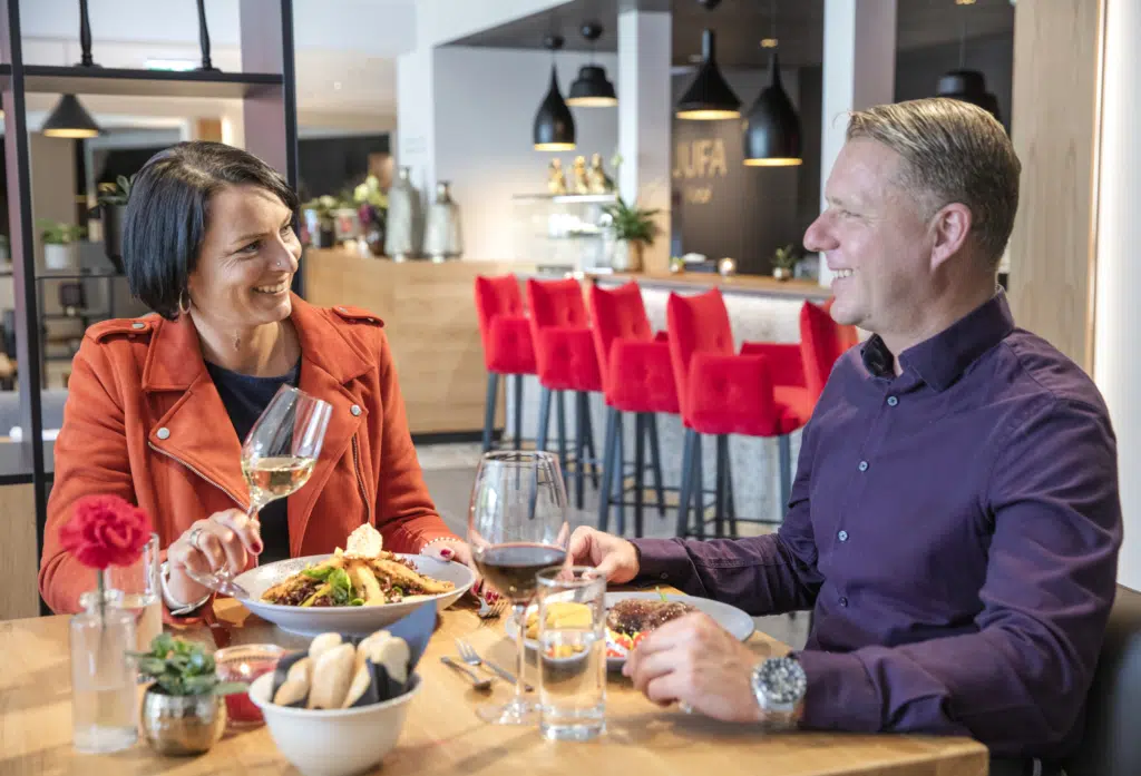 Sie sehen ein Paar beim Abendessen in der Lounge im JUFA Hotel Salzburg City. Der Ort für erholsamen Familienurlaub und einen unvergesslichen Winter- und Wanderurlaub.