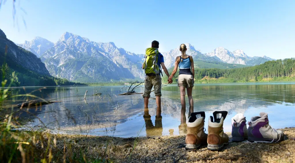 Ein junges Paar steht im Sommer händehaltend im Almsee im Almtal. JUFA Hotels bietet Ihnen den Ort für erlebnisreichen Natururlaub für die ganze Familie.