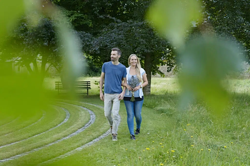 Ihr seht ein Paar bei einem Spaziergang am JUFA Hotel Stift Gurk im Sommer. JUFA Hotels bietet den Ort für erlebnisreichen Natururlaub für die ganze Familie.