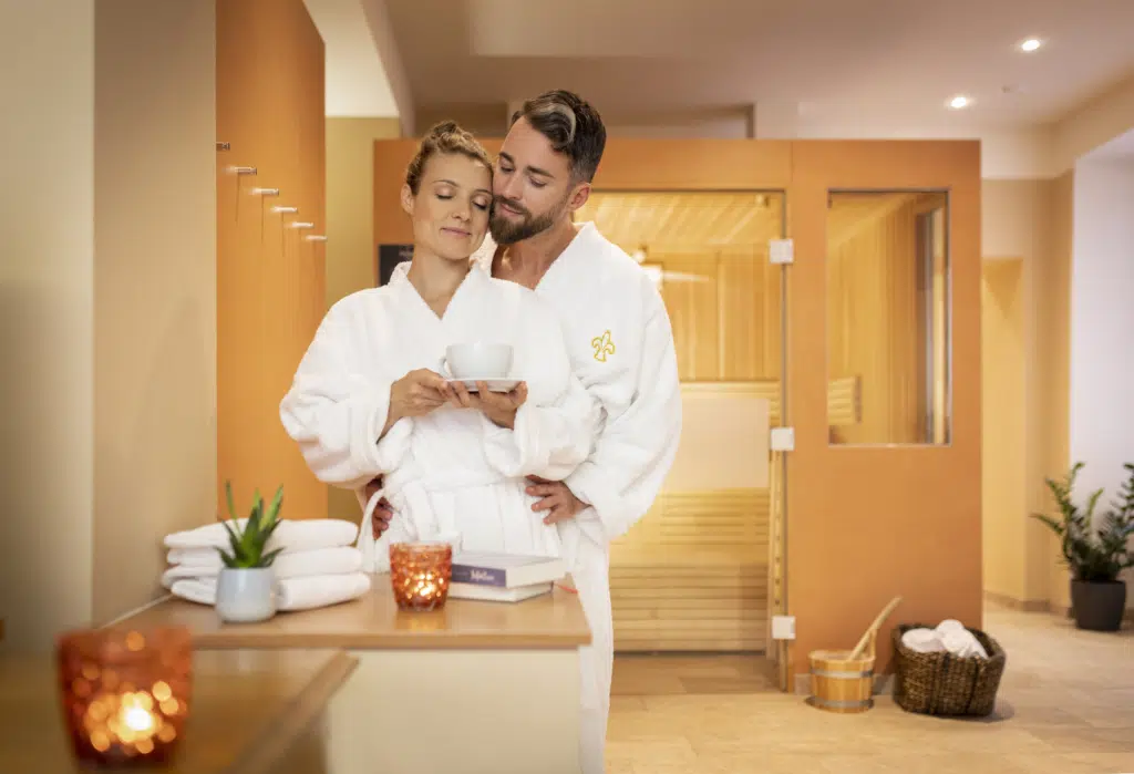 Ihr seht ein Pärchen im Wellness Bereich. Die Frau hält eine Kaffee Tee in der Hand. JUFA Hotels bietet erholsamen Familienurlaub und einen unvergesslichen Winter- und Wanderurlaub.