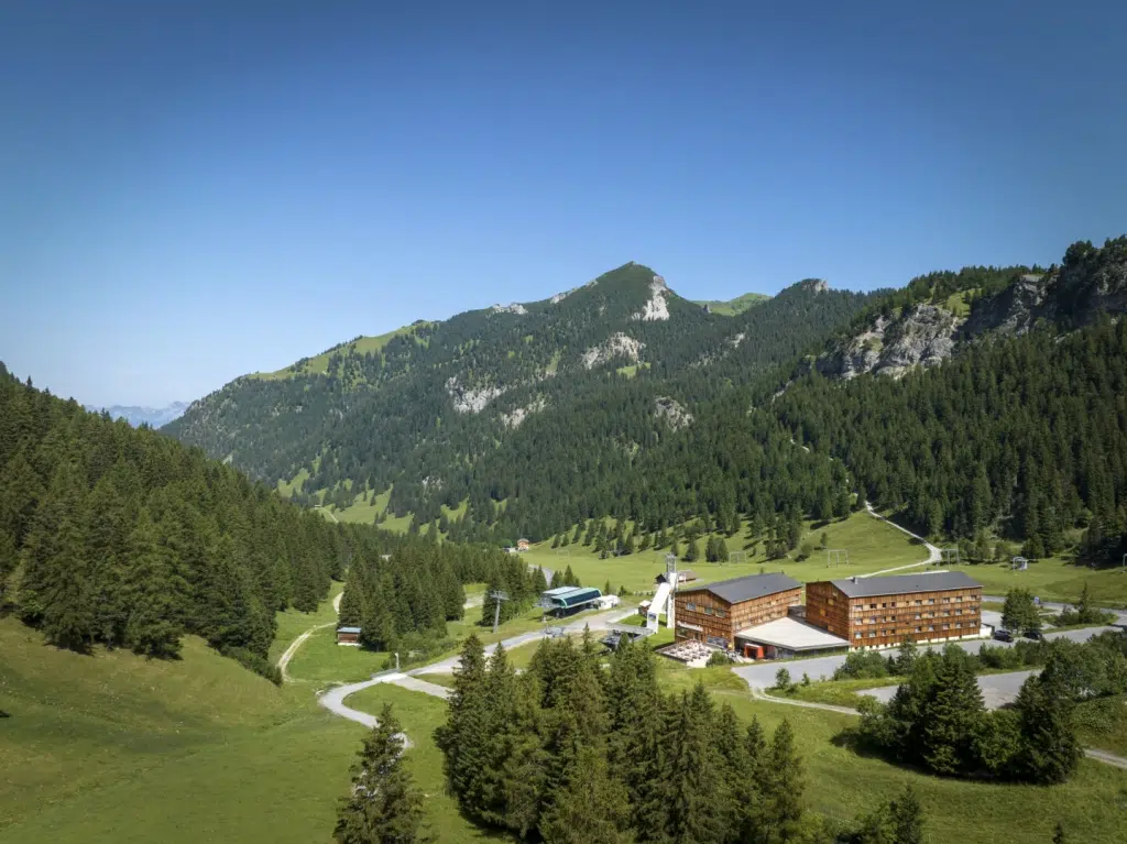 Ihr seht die Aussenansicht des JUFA Hotels Malbun mit dem Bergmassiv im Hintergrund