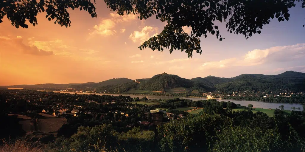 Ihr seht eine Panoramaaufnahme des Siebengebirges mit Rhein im Vordergrund bei Sonnenuntergang. JUFA Hotels bietet erlebnisreiche Städtetrips für die ganze Familie und den idealen Platz für Ihr Seminar.