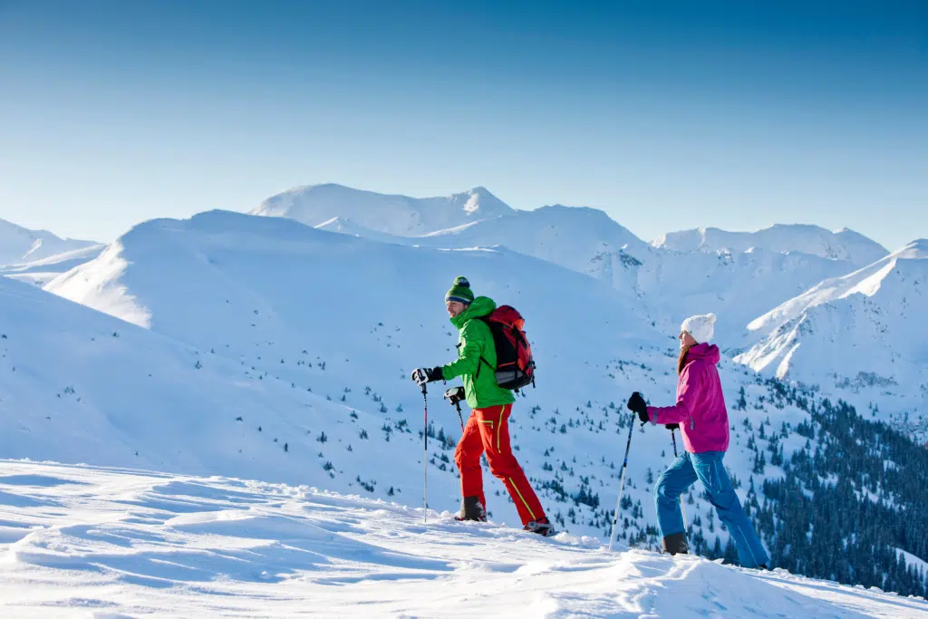 Ihr seht ein Paar beim schneeschuhwandern im Winter auf der Planneralm mit Bergen im Hintergrund. JUFA Hotels bietet erholsamen Familienurlaub und einen unvergesslichen Winterurlaub.