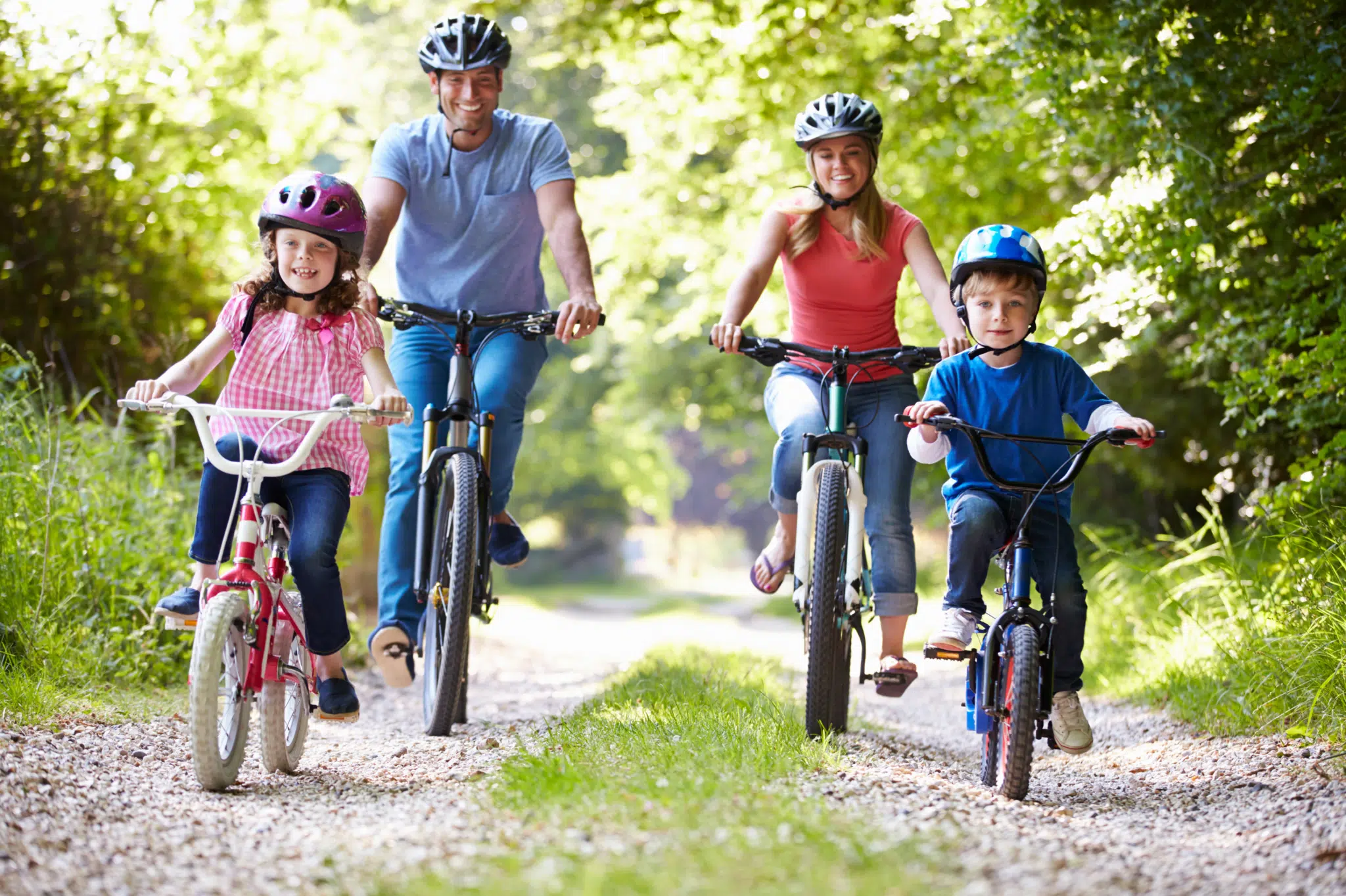 Ihr seht zwei Erwachsene und zwei Kinder auf Fahrrädern durch den Wald fahren. JUFA Hotels bietet kinderfreundlichen und erlebnisreichen Urlaub für die ganze Familie.