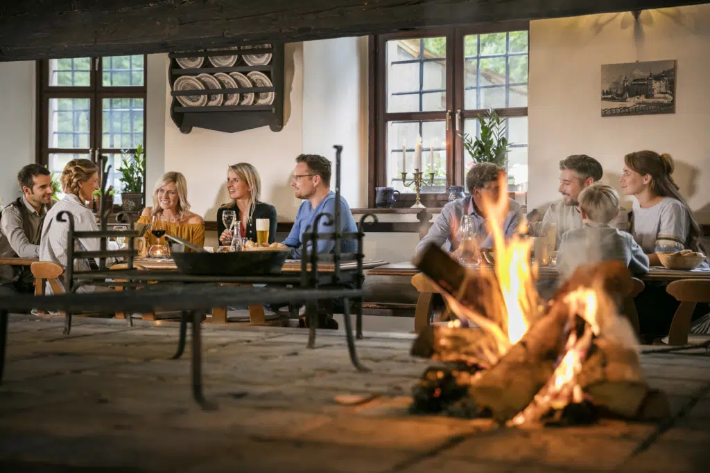 Ihr seht Gäste in der Rauchkuchl mit Feuer sitzen im JUFA Hotel Schloss Röthelstein/Admont***. Der Ort für märchenhafte Hochzeiten und erfolgreiche und kreative Seminare.