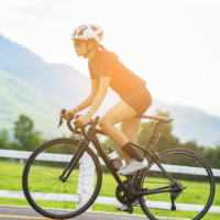 Sie sehen eine Frau am Rennrad, die einen Hügel mit grüner Wiese hinauf radelt