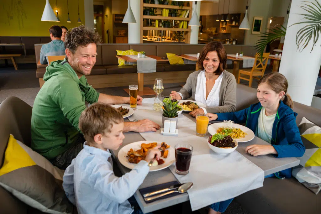 Ihr seht eine Familie beim Essen der Köstlichkeiten aus der Hotelküche im JUFA Kempten. Der Ort für kinderfreundlichen und erlebnisreichen Urlaub für die ganze Familie.