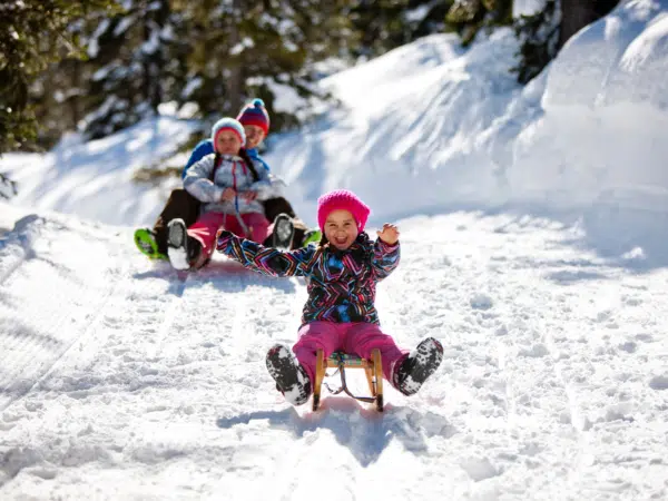 Ihr seht eine Familie mit Schlitten im Winter beim rodeln auf der Planneralm. JUFA Hotels bietet erholsamen Familienurlaub und einen unvergesslichen Winterurlaub.