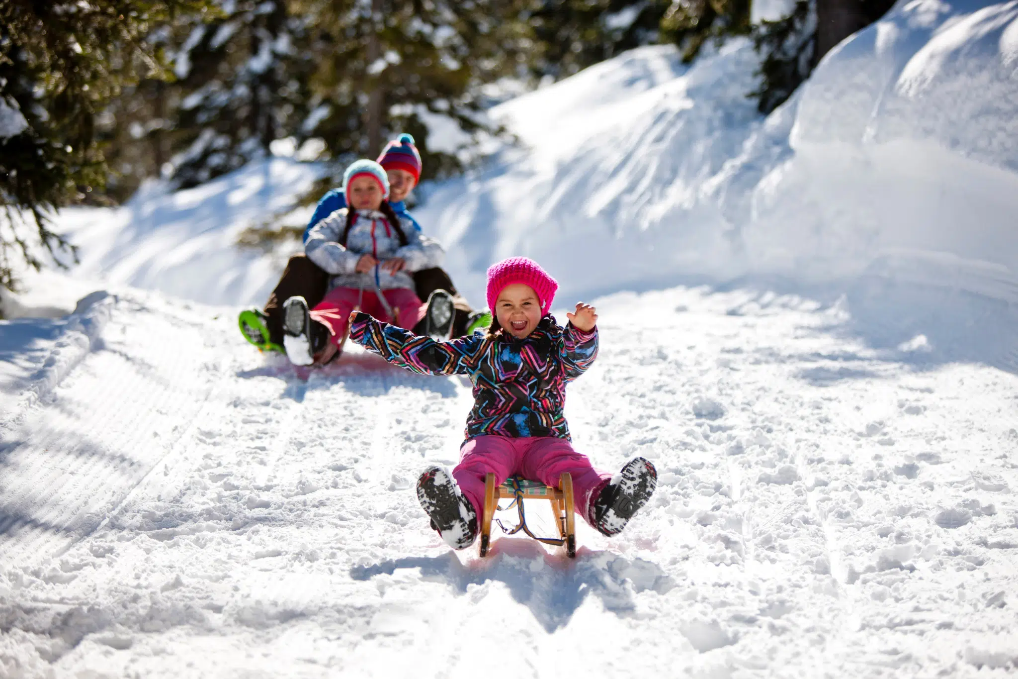 Ihr seht eine Familie mit Schlitten im Winter beim rodeln auf der Planneralm. JUFA Hotels bietet erholsamen Familienurlaub und einen unvergesslichen Winterurlaub.