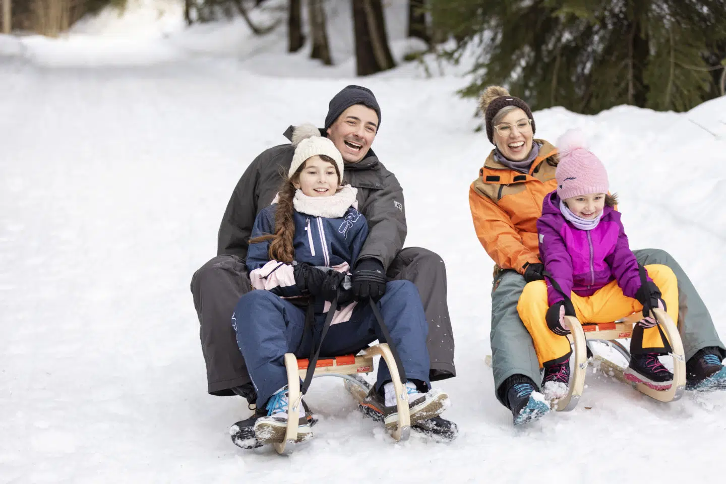 Sie sehen eine Familie beim Schlittenfahren durch den Wald. Das JUFA Hotel Laterns – Klangholzhus ist ein idealer Ort für einen unvergesslichen Winter- und Familienurlaub und erholsame Tage für die ganze Familie.