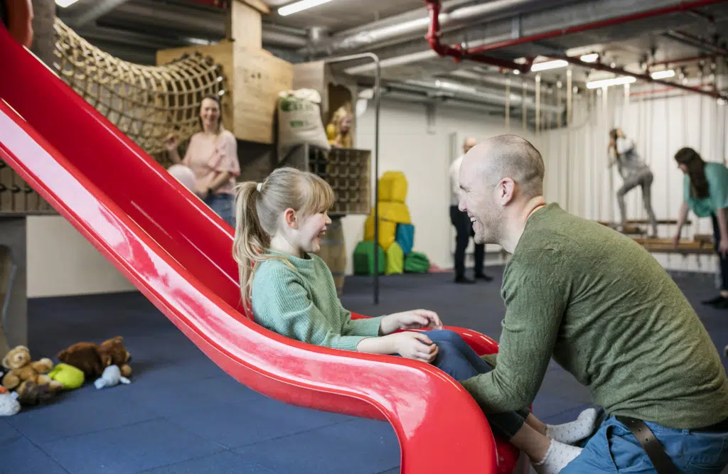 Ihr seht Kinder mit ihren Eltern im Indoor-Spielbereich des JUFA Hotels Hamburg HafenCity****. Der Ort für kinderfreundlichen und erlebnisreichen Urlaub für die ganze Familie.