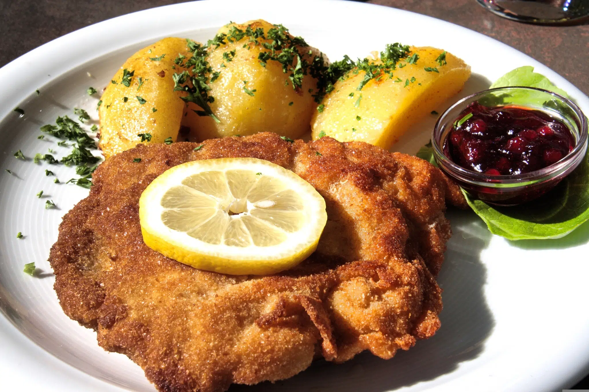 Ihr seht ein Wiener Schnitzel mit Petersilienkartoffeln, Preiselbeermarmelade und einer Zitronenscheibe.