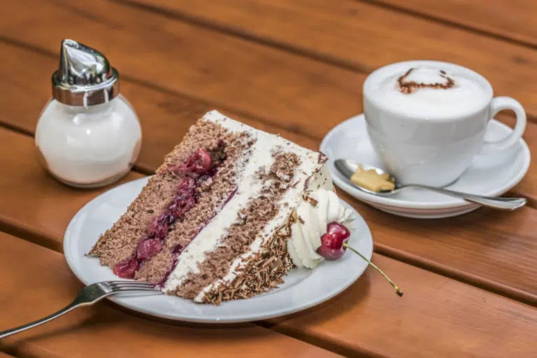 Ihr seht die Schwarzwälder Kirschtorte, ein kulinarisches Highlight der Region mit Kaffee und Zucker im Hintergrund