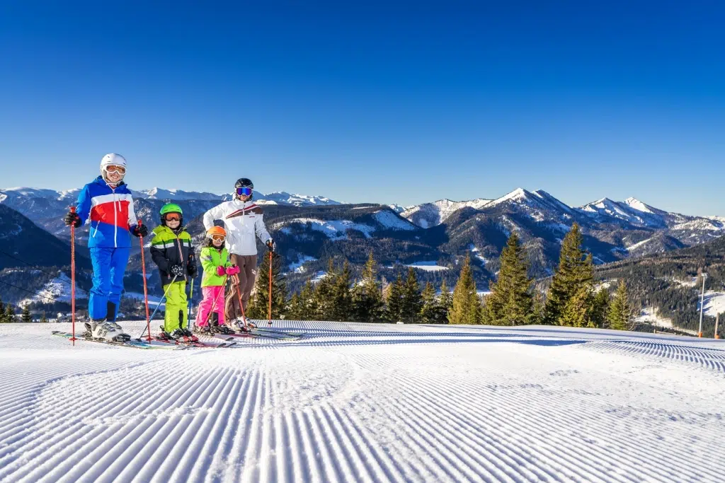 Ihr seht eine Familie beim Skifahren auf der Bürgeralpe mit perfekt präparieren Pisten im Mariazeller Land.