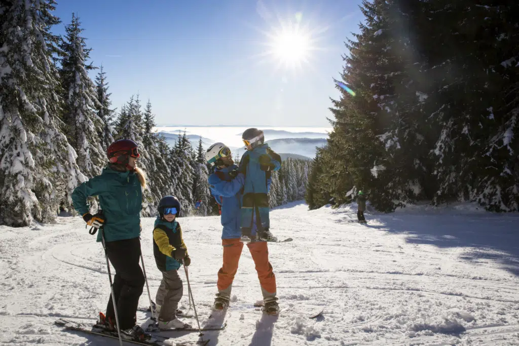 Ihr seht eine Familie beim Skifahren im Schwarzwald mit winterlicher Kulisse im Hintergrund.