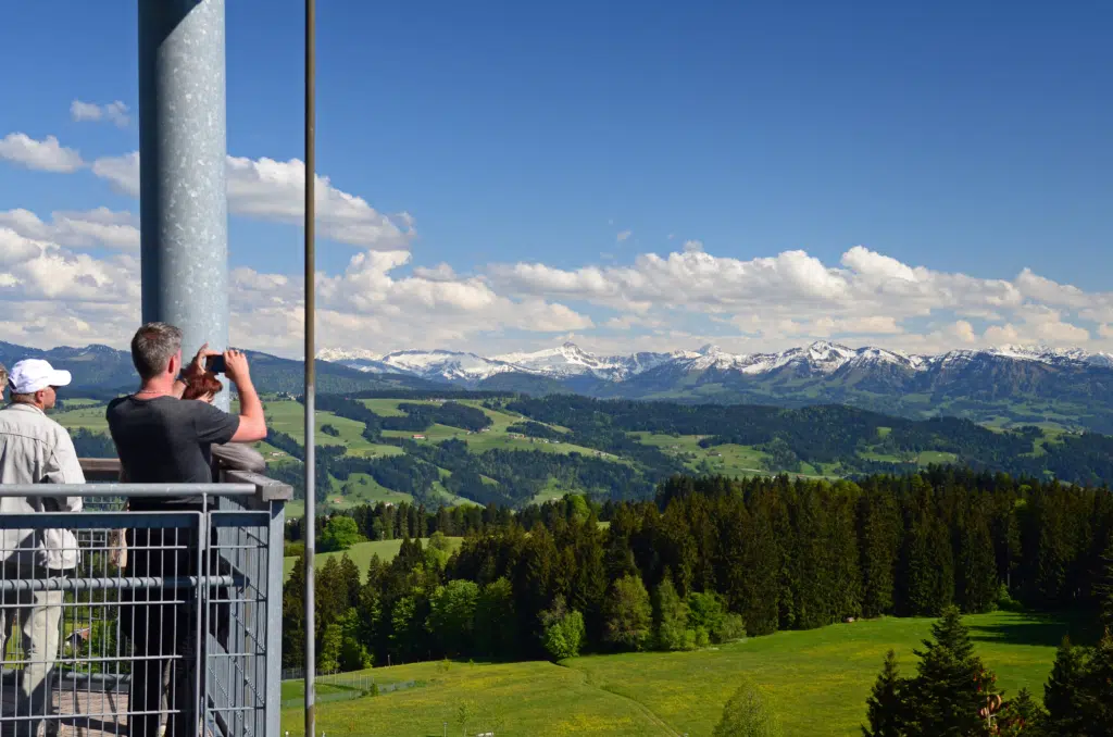 Ihr seht Wanderer, die das tolle Bergpanorama am Skywalk Allgäu in Scheidegg in Bayern genießen. JUFA Hotels bieten erholsamen Familienurlaub und einen unvergesslichen Winter- und Wanderurlaub.