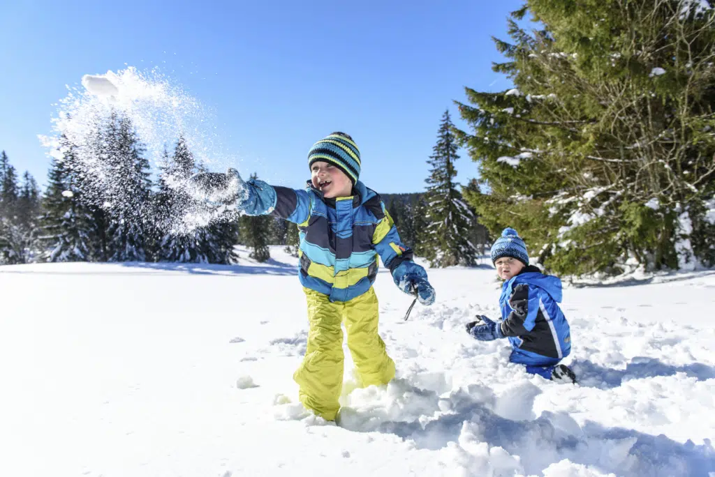 Ihr seht zwei spielende Kinder im Schnee kniend und lachend.