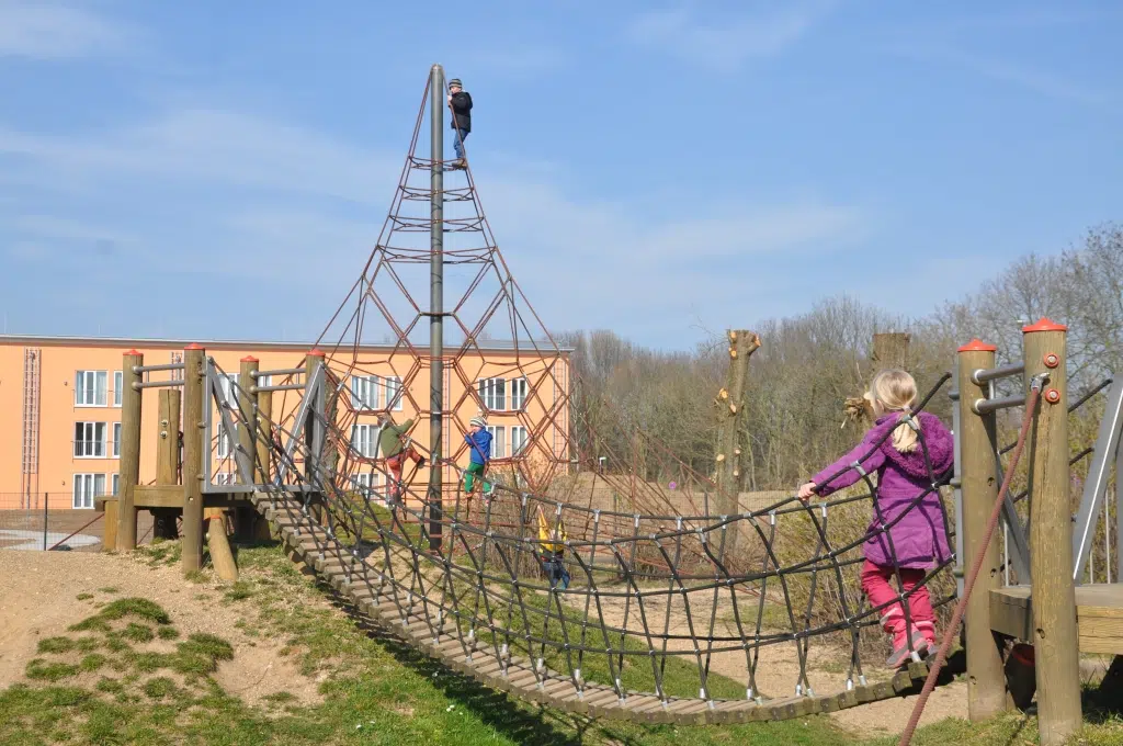 Ihr seht ein Kind, das über eine Hängebrücke am Spielplatz am JUFA Hotel Jülich***s geht. Der Ort für kinderfreundlichen und erlebnisreichen Urlaub für die ganze Familie.