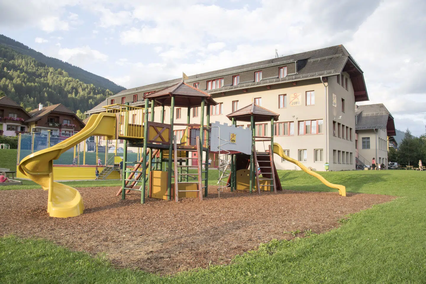 Spielplatz mit Kletterburg und Riesentrampolin beim JUFA Hotel Lungau im Sommer.