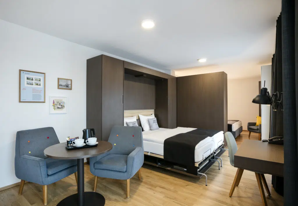 Ihr seht ein Doppelbett und eine Sitzmöglichkeit in einer Suite im JUFA Hotel Hamburg HafenCity****. Der Ort für erlebnisreichen Städtetrip für die ganze Familie und der ideale Platz für Ihr Seminar.