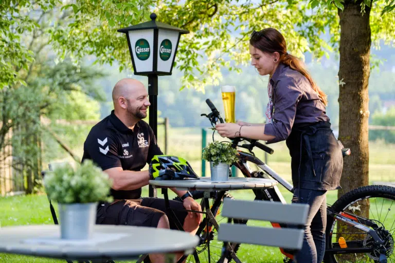 Ihr seht einen Mann im Gastgarten nach einer Fahrradtour im JUFA Hotel Lipizzanerheimat***. Der Ort für erlebnisreichen Natururlaub für die ganze Familie.