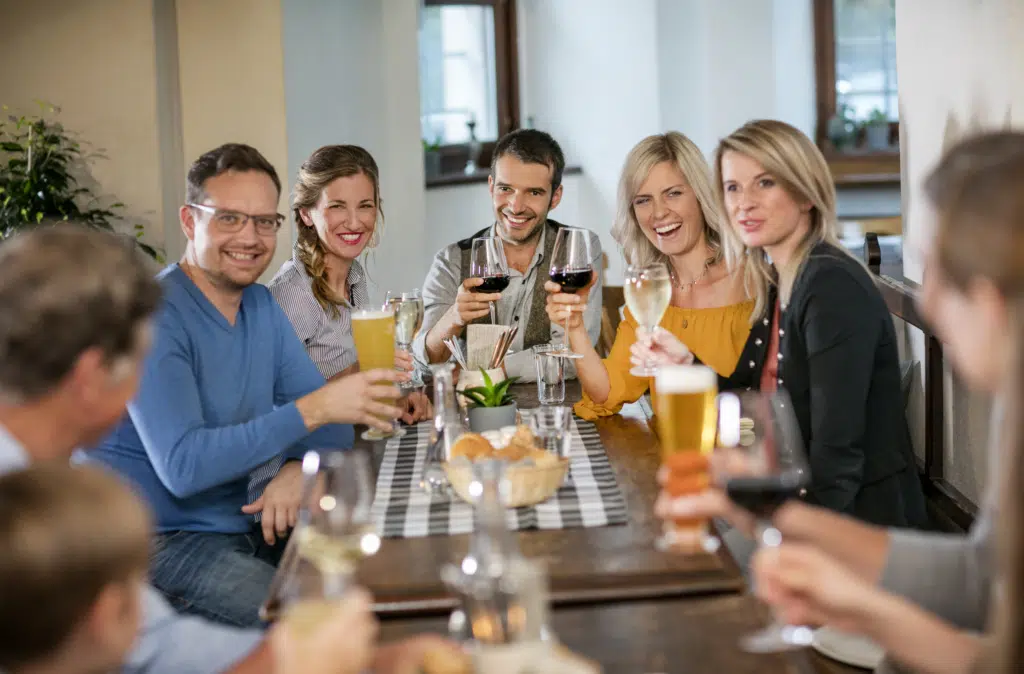 Ihr seht Gäste in der Rauchkuchl des JUFA Hotel Schloss Röthelstein/Admont*** am Tisch sitzen und mit Getränken anstoßen. JUFA Hotels bietet den Ort für märchenhafte Hochzeiten und erfolgreiche und kreative Seminare.