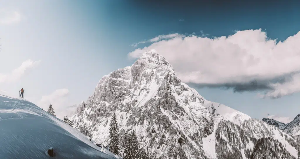 Ihr seht einen Skitourengeher im Gebirge des Nationalparks Gesäuse durch den Schnee steigen.