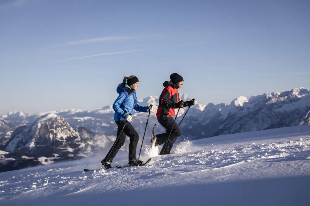 Ihr seht zwei Personen beim Schneeschugehen im Winter.