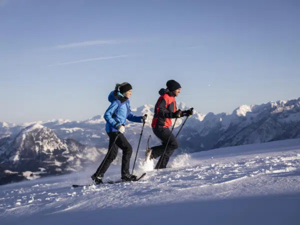 Ihr seht zwei Personen beim Schneeschugehen im Winter.