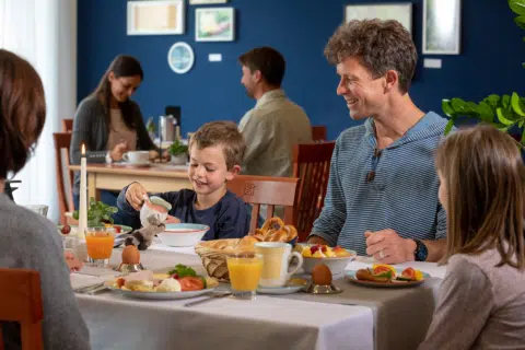 Ihr seht eine Familie mit zwei Kindern beim Frühstück mit Ei und Cornflakes im JUFA Hotel Nördlingen***. Der Ort für kinderfreundlichen und erlebnisreichen Urlaub für die ganze Familie.