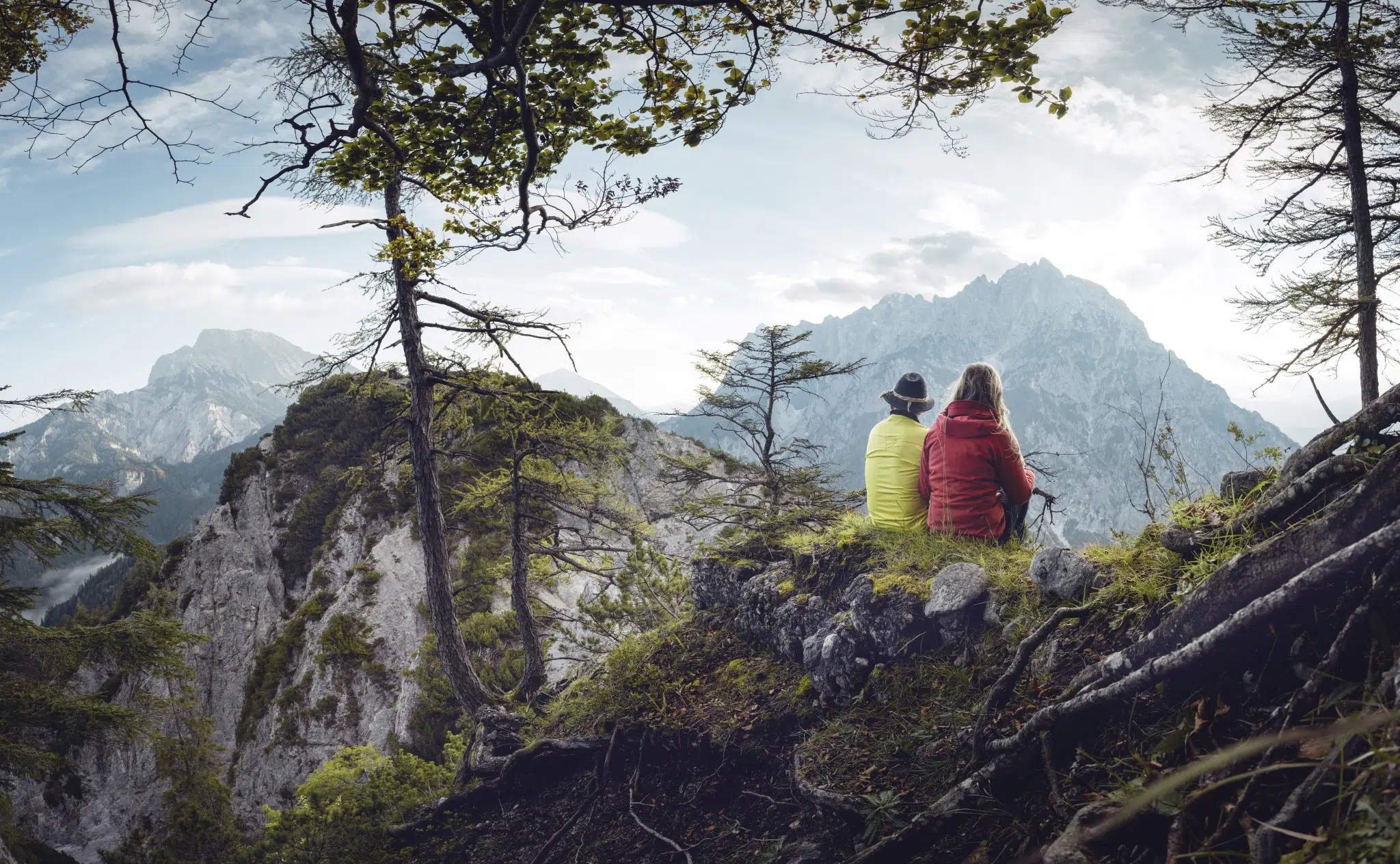 Ihr seht ein Paar, das eine Wanderpause mit atemberaubenden Ausblick genießt. JUFA Hotels bietet euch den Ort für erlebnisreichen Natururlaub für die ganze Familie.