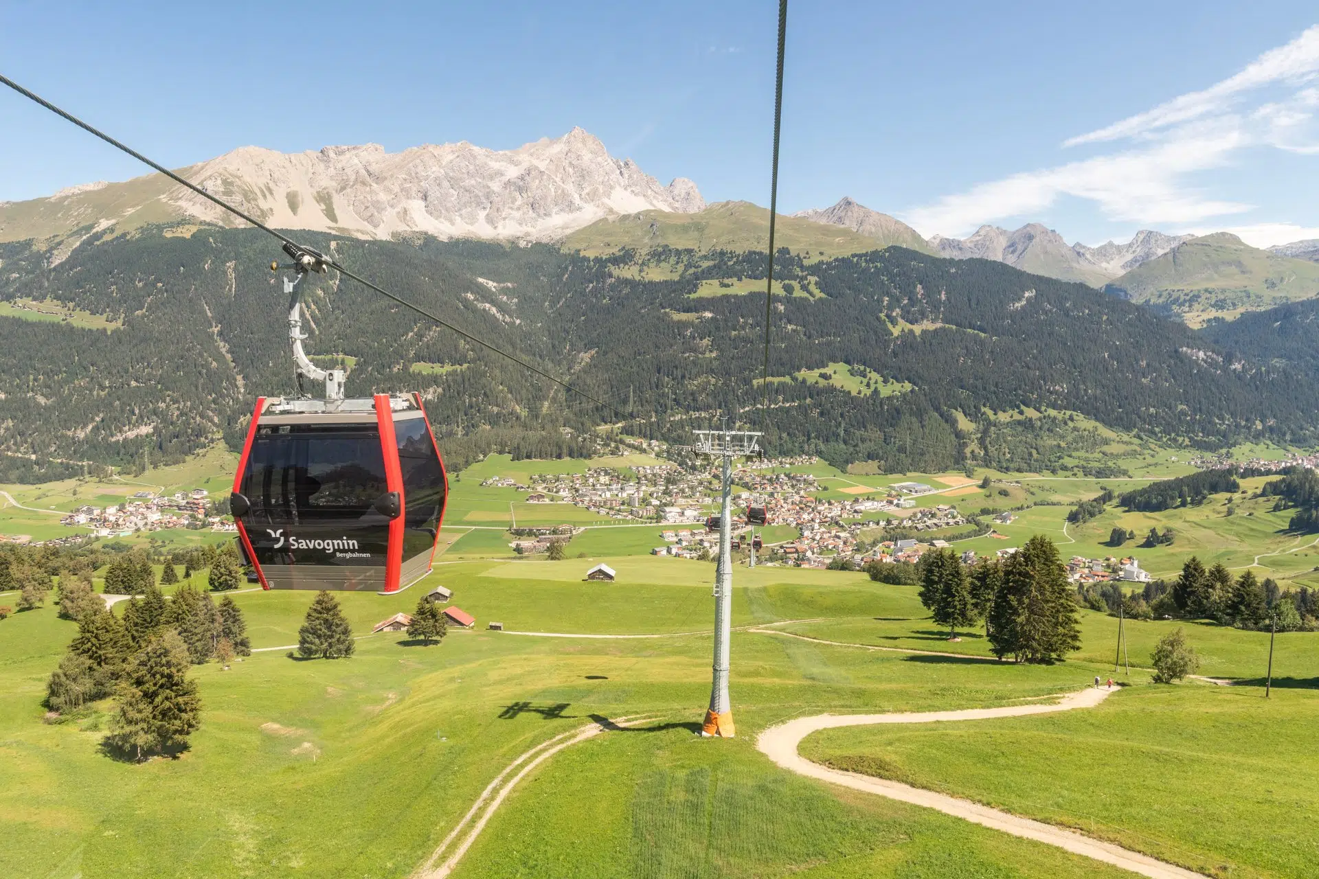 Ihr seht die Bergbahnen Savognin im Sommer über die Stadt Savognin schweben